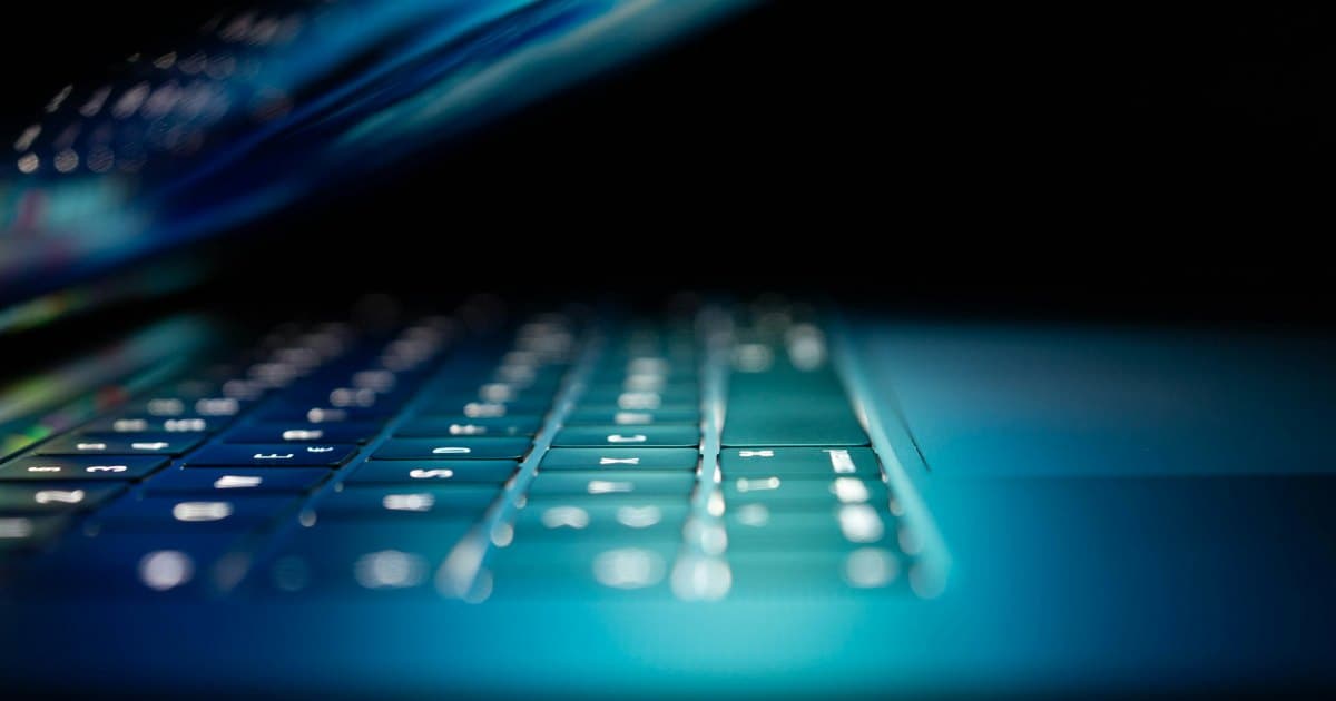 Laptop keyboard lit by cyan and blue light in a dark room
