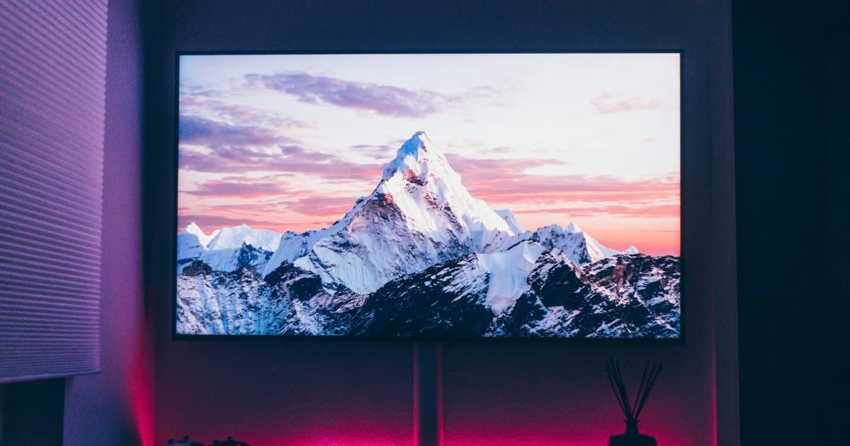 Wall-mounted TV in a dark room showing a snow-capped mountain, with ambient LED light glowing behind the TV stand